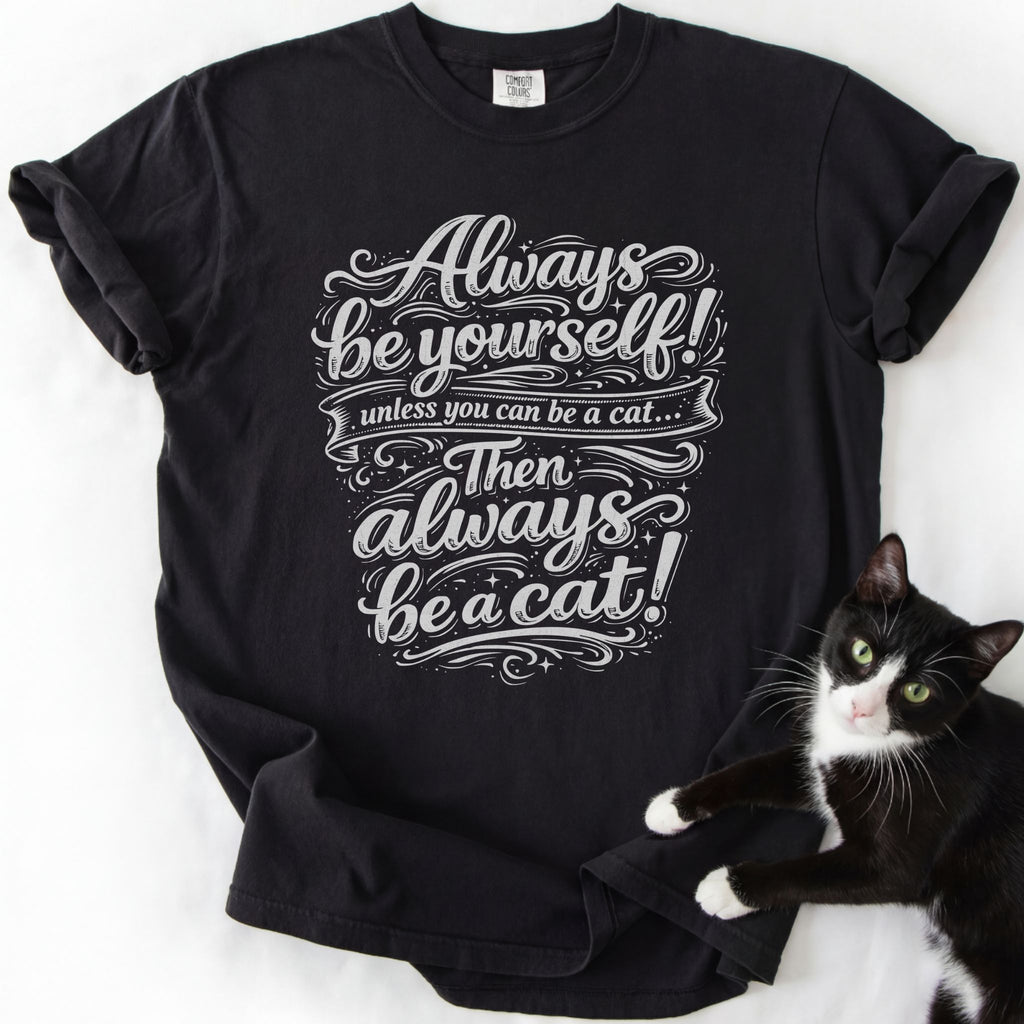 Black funny cat t-shirt with "Always Be a Cat" ornate script and star motifs — front view