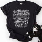 Black funny cat t-shirt with "Always Be a Cat" ornate script and star motifs — front view
