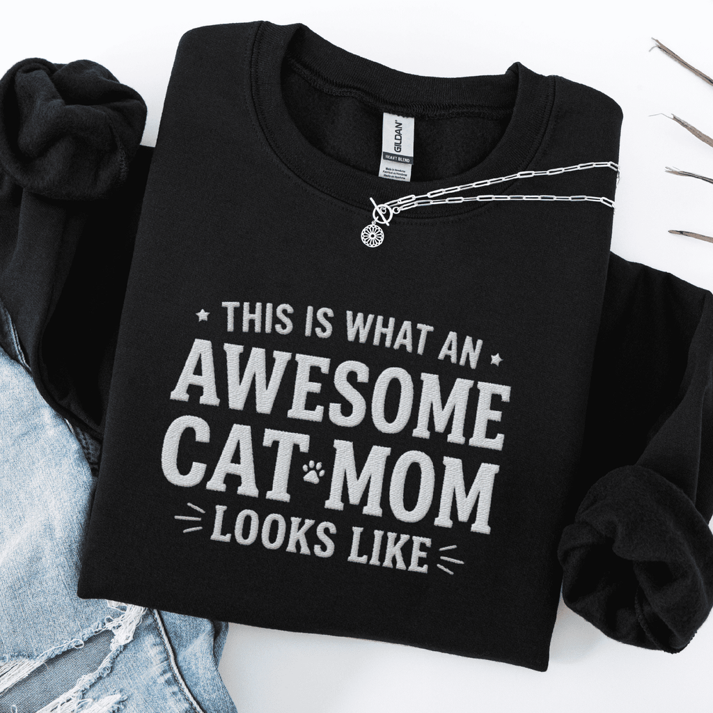 Black awesome cat mom embroidered sweatshirt with “This Is What An Awesome Cat Mom Looks Like” text, folded flat on light denim