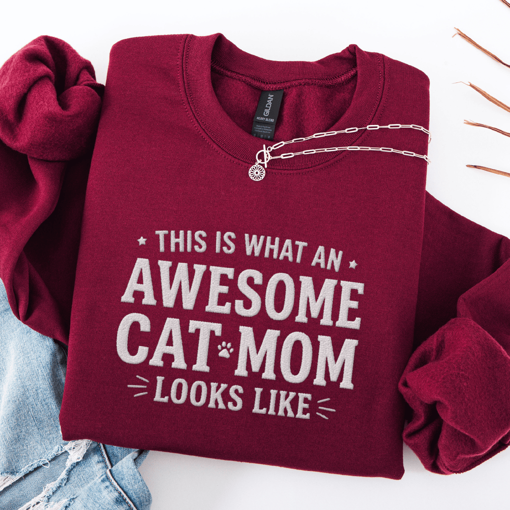 Maroon awesome cat mom embroidered sweatshirt with “This Is What An Awesome Cat Mom Looks Like” text, folded flat on light denim
