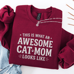Maroon awesome cat mom embroidered sweatshirt with “This Is What An Awesome Cat Mom Looks Like” text, folded flat on light denim