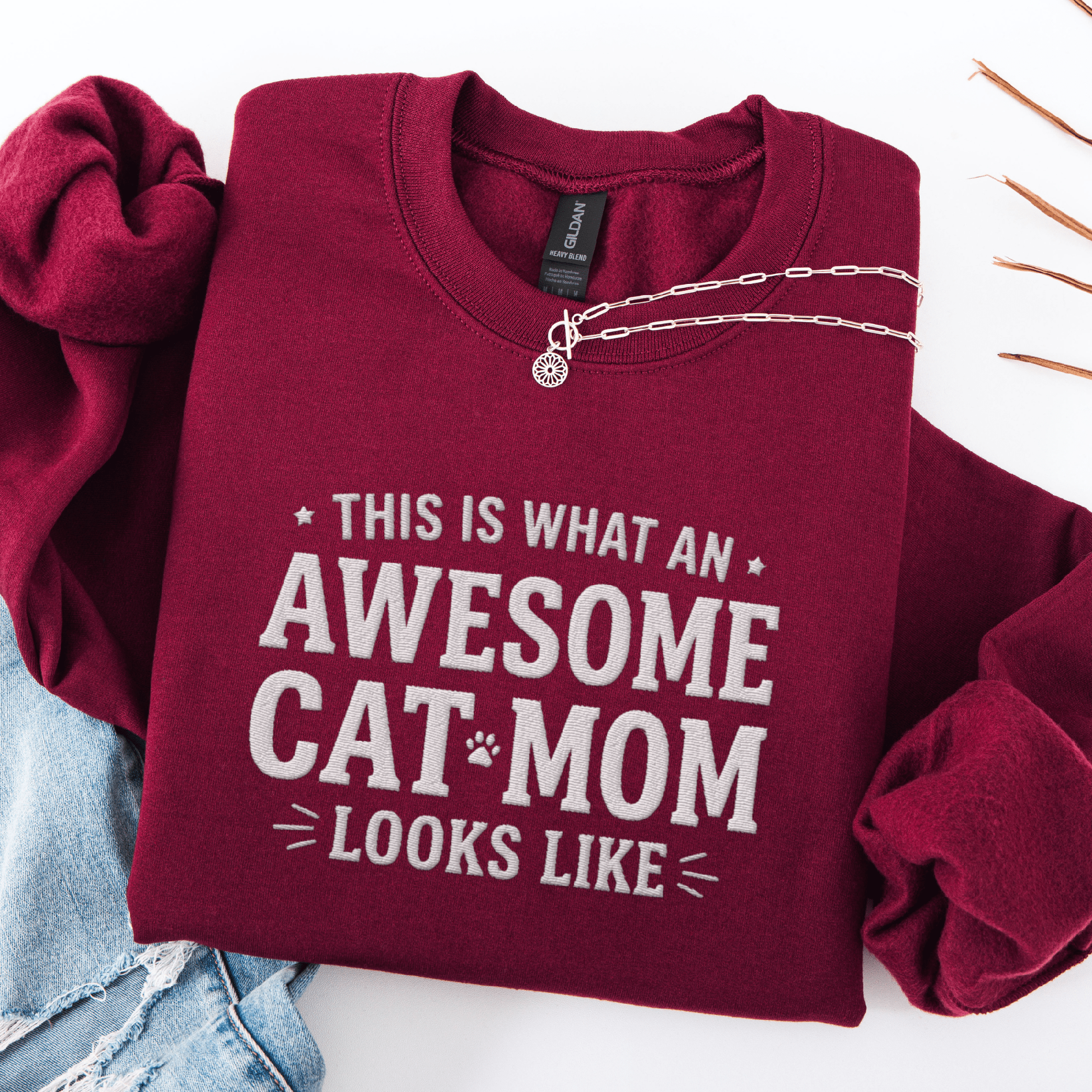 Maroon awesome cat mom embroidered sweatshirt with “This Is What An Awesome Cat Mom Looks Like” text, folded flat on light denim