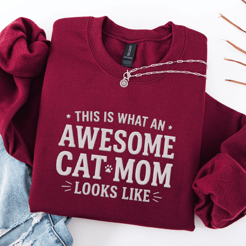 Maroon awesome cat mom embroidered sweatshirt with “This Is What An Awesome Cat Mom Looks Like” text, folded flat on light denim
