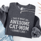 Dark Heather awesome cat mom embroidered sweatshirt with “This Is What An Awesome Cat Mom Looks Like” text, folded flat on light denim