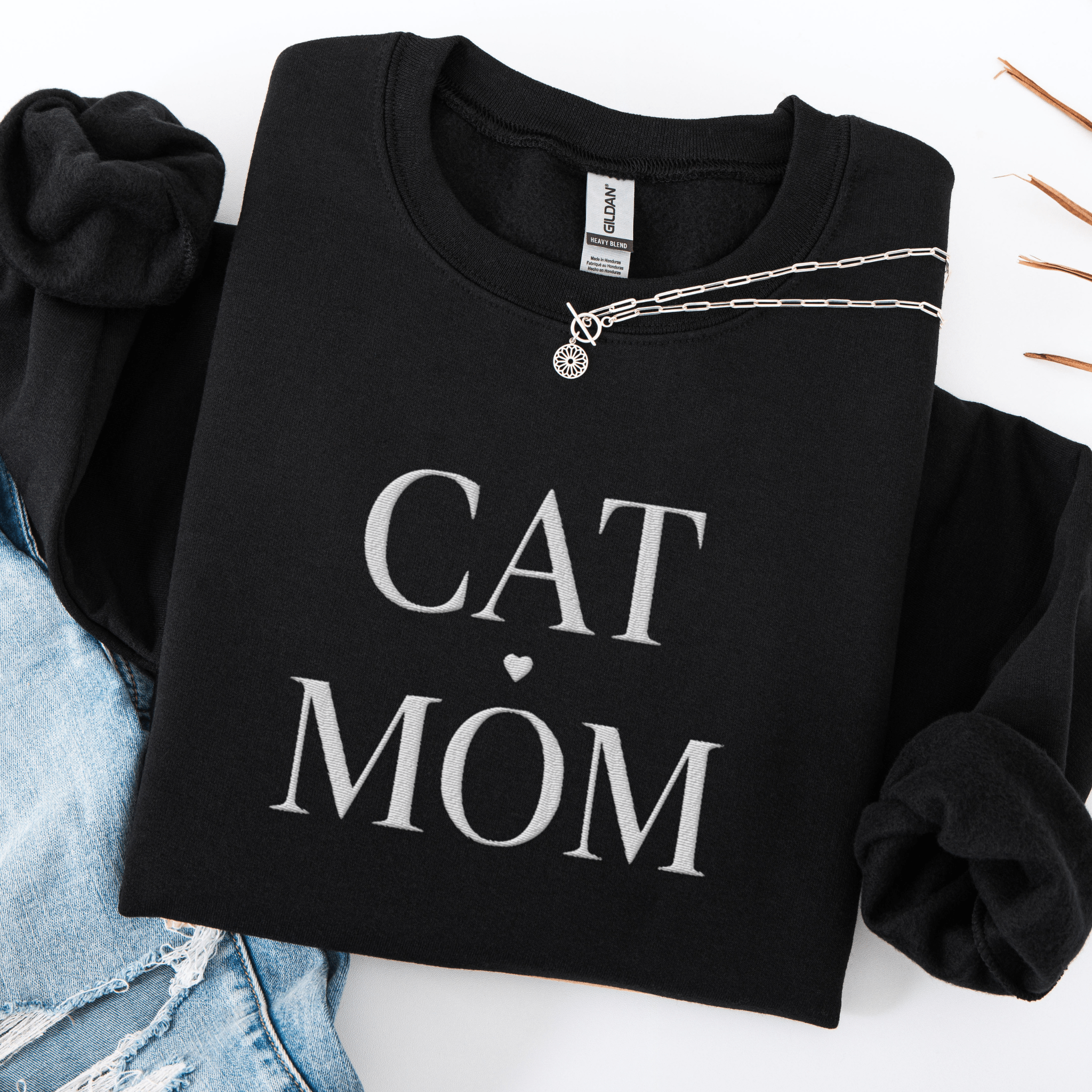 Black cat mom embroidered sweatshirt, folded flat on light denim