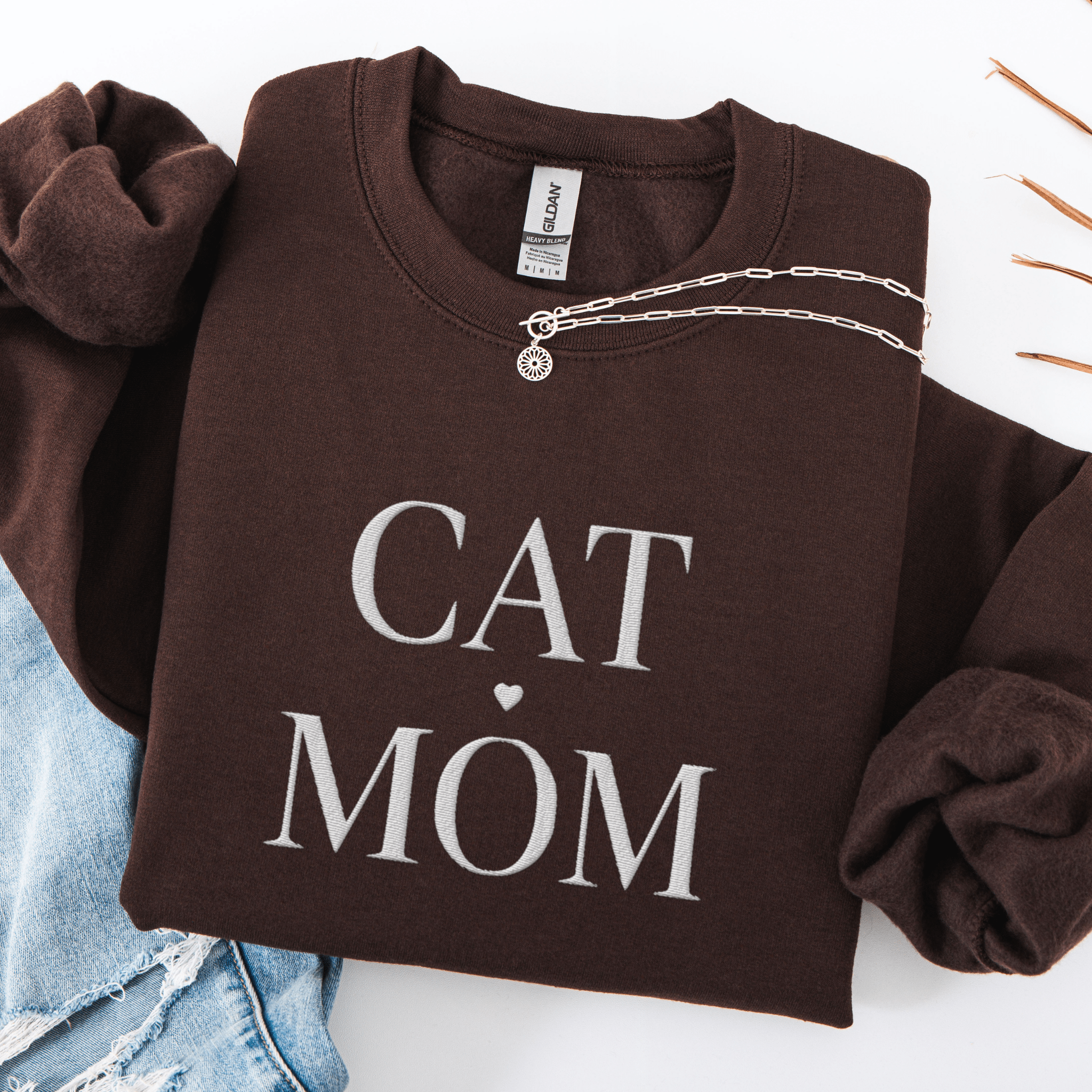 Dark Chocolate cat mom embroidered sweatshirt, folded flat on light denim