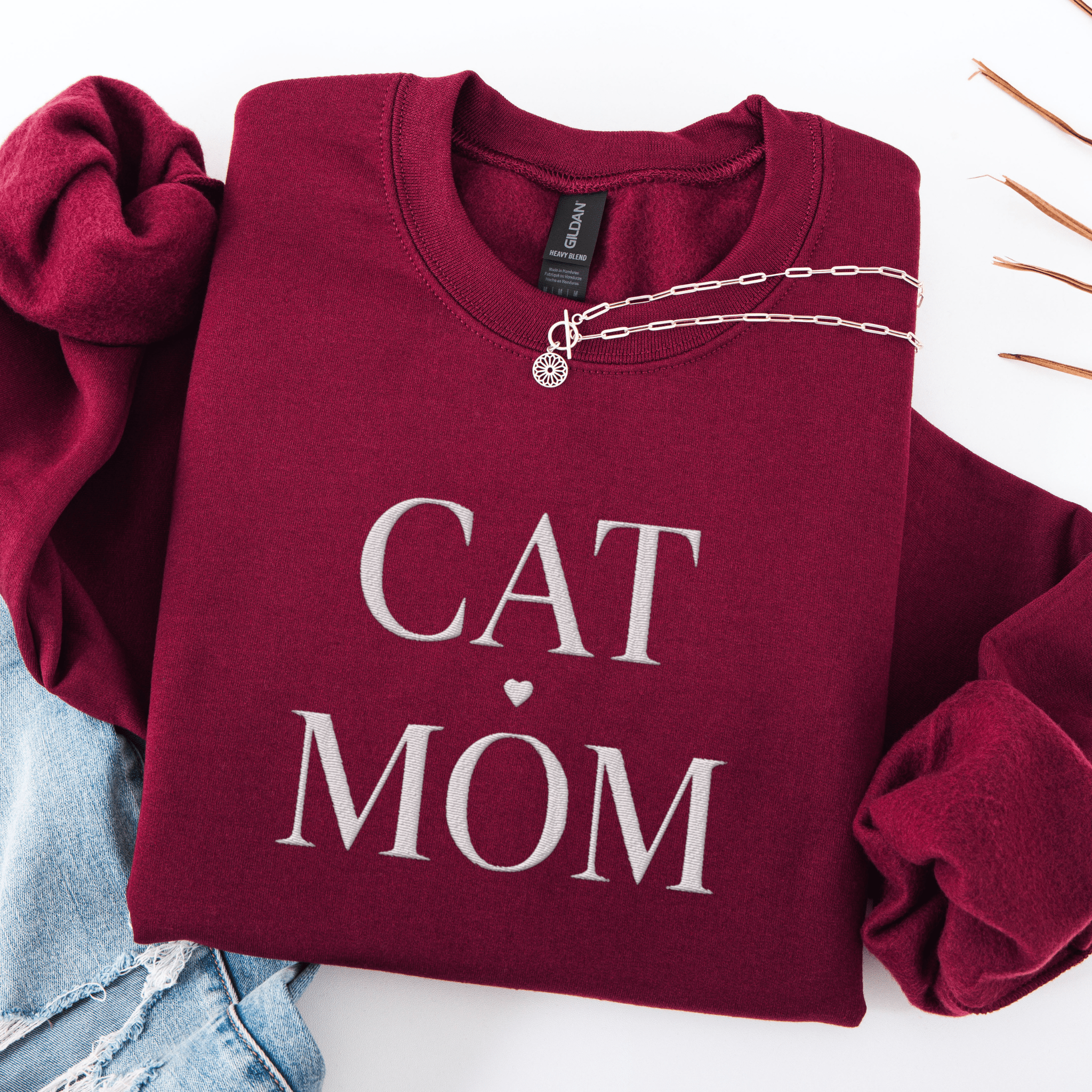 Maroon cat mom embroidered sweatshirt, folded flat on light denim