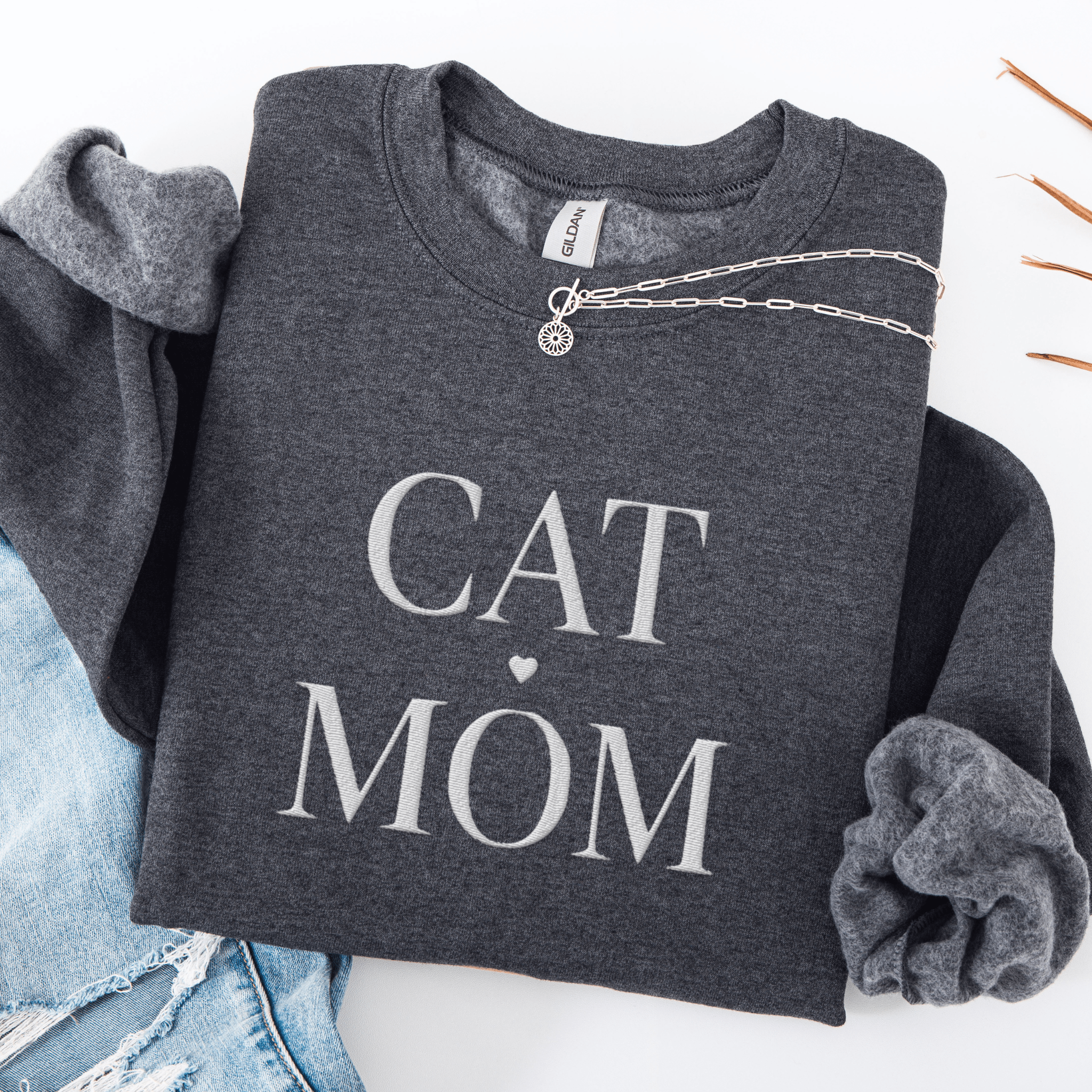 Dark Heather cat mom embroidered sweatshirt, folded flat on light denim