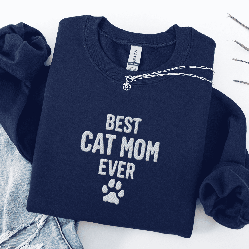 Navy best cat mom ever embroidered sweatshirt with paw print detail, folded flat on light denim