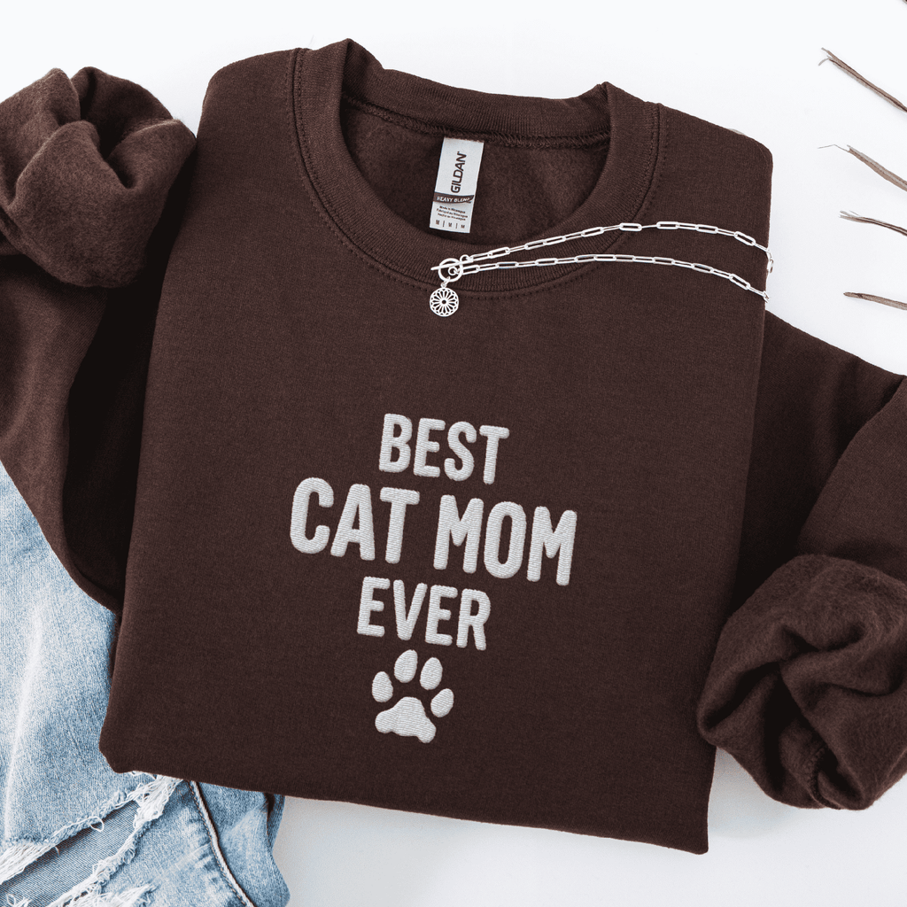 Dark Chocolate best cat mom ever embroidered sweatshirt with paw print detail, folded flat on light denim