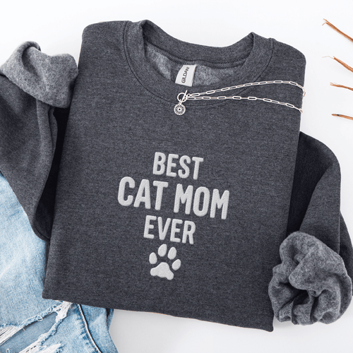 Dark Heather best cat mom ever embroidered sweatshirt with paw print detail, folded flat on light denim