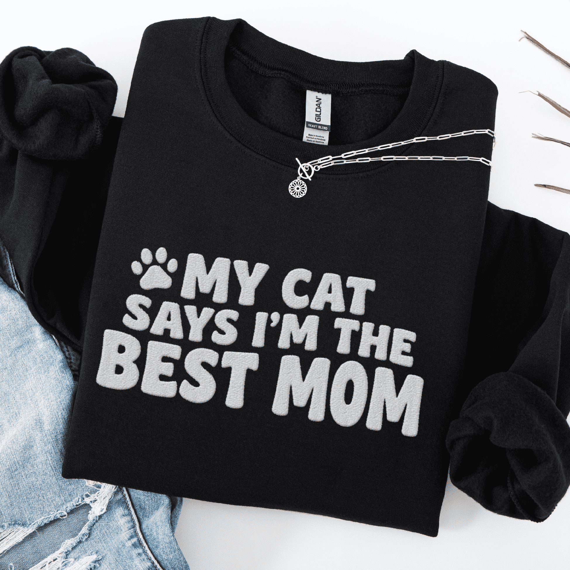 Black cat mom embroidered sweatshirt with “My Cat Says I’m The Best Mom” text, folded flat on light denim