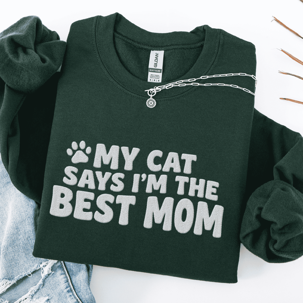 Forest Green cat mom embroidered sweatshirt with “My Cat Says I’m The Best Mom” text, folded flat on light denim