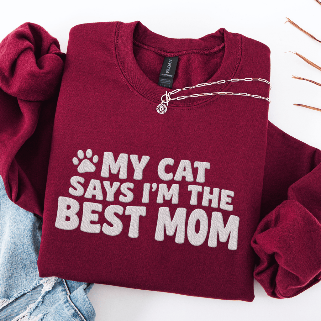 Maroon cat mom embroidered sweatshirt with “My Cat Says I’m The Best Mom” text, folded flat on light denim