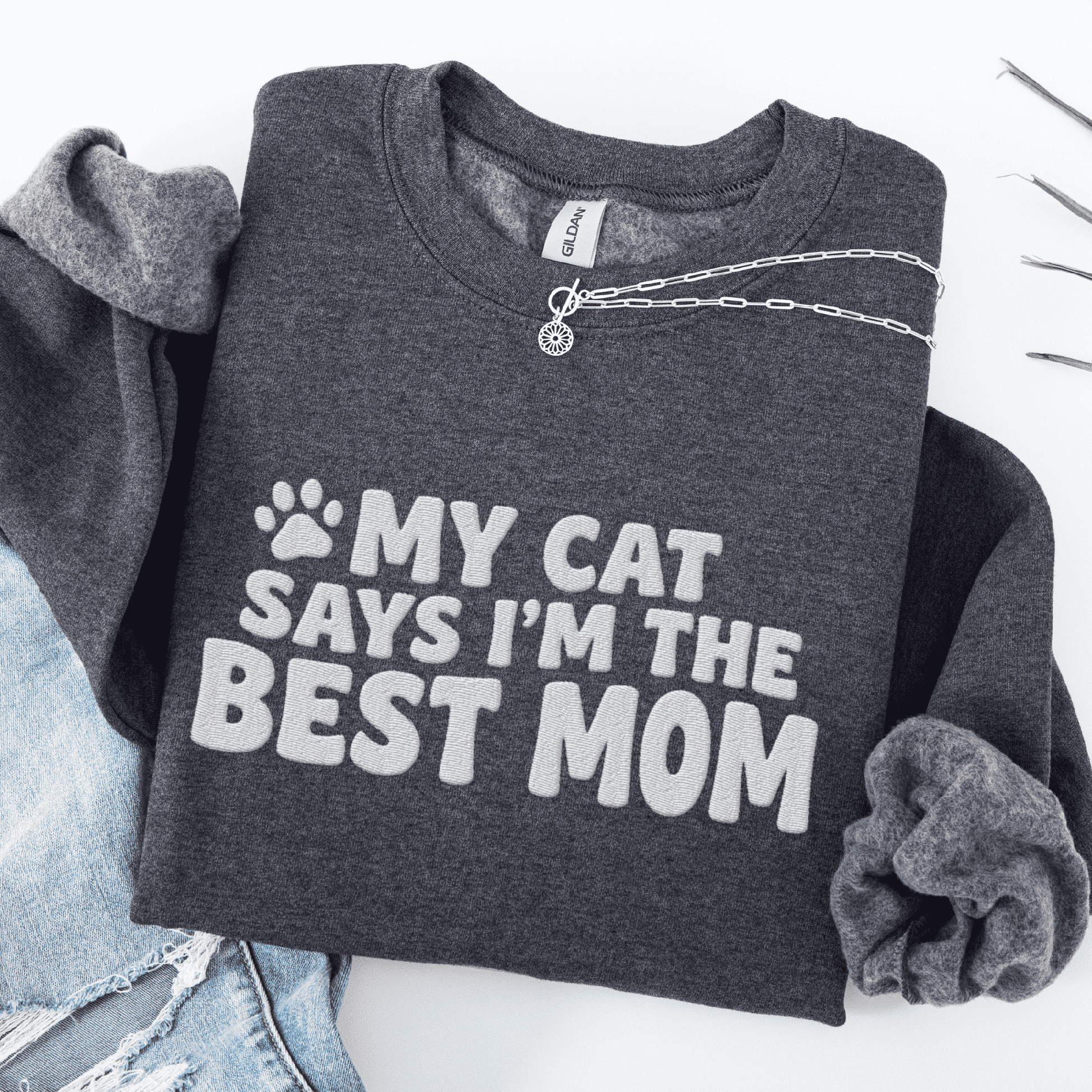 Dark Heather cat mom embroidered sweatshirt with “My Cat Says I’m The Best Mom” text, folded flat on light denim