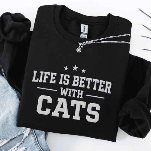 Black cat embroidered sweatshirt with “Life Is Better With Cats” text, folded flat on light denim