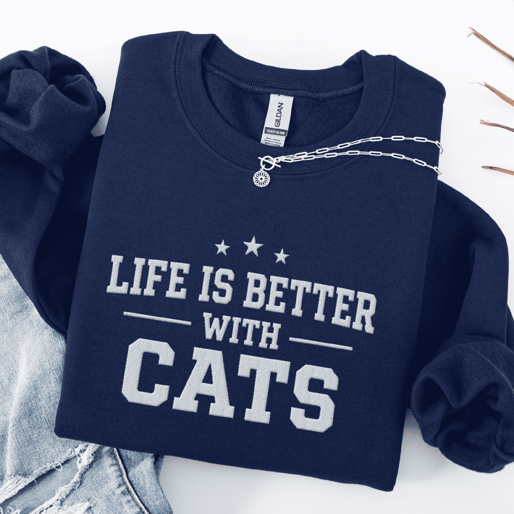 Navy cat embroidered sweatshirt with “Life Is Better With Cats” text, folded flat on light denim