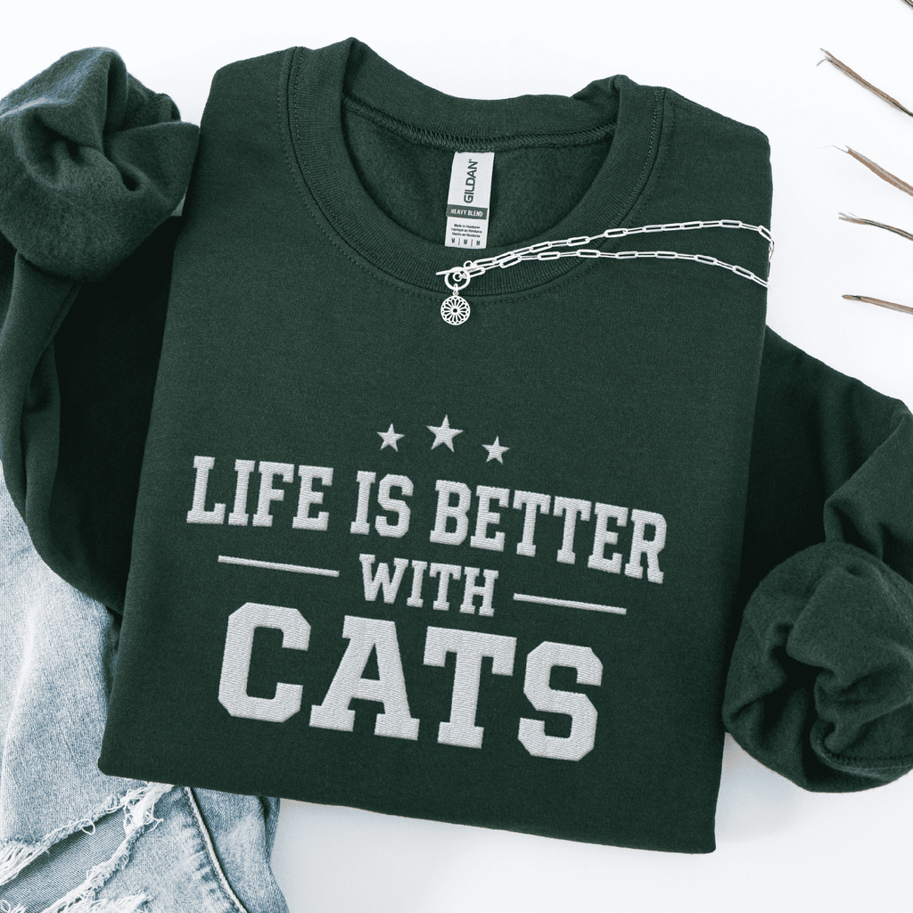 Forest Green cat embroidered sweatshirt with “Life Is Better With Cats” text, folded flat on light denim