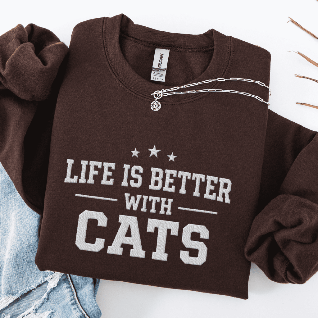 Dark Chocolate cat embroidered sweatshirt with “Life Is Better With Cats” text, folded flat on light denim