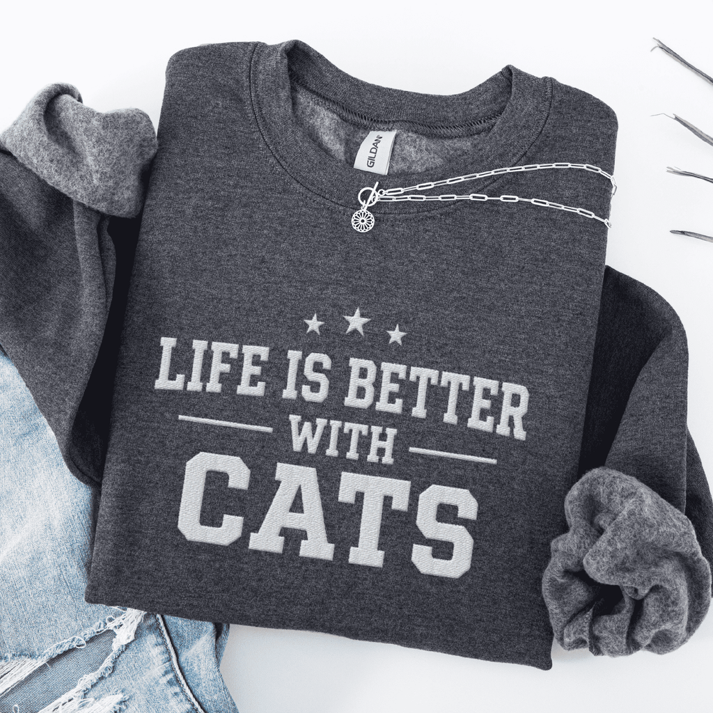 Dark Heather cat embroidered sweatshirt with “Life Is Better With Cats” text, folded flat on light denim