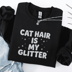 Black cat embroidered sweatshirt with “Cat Hair Is My Glitter” text, folded flat on light denim