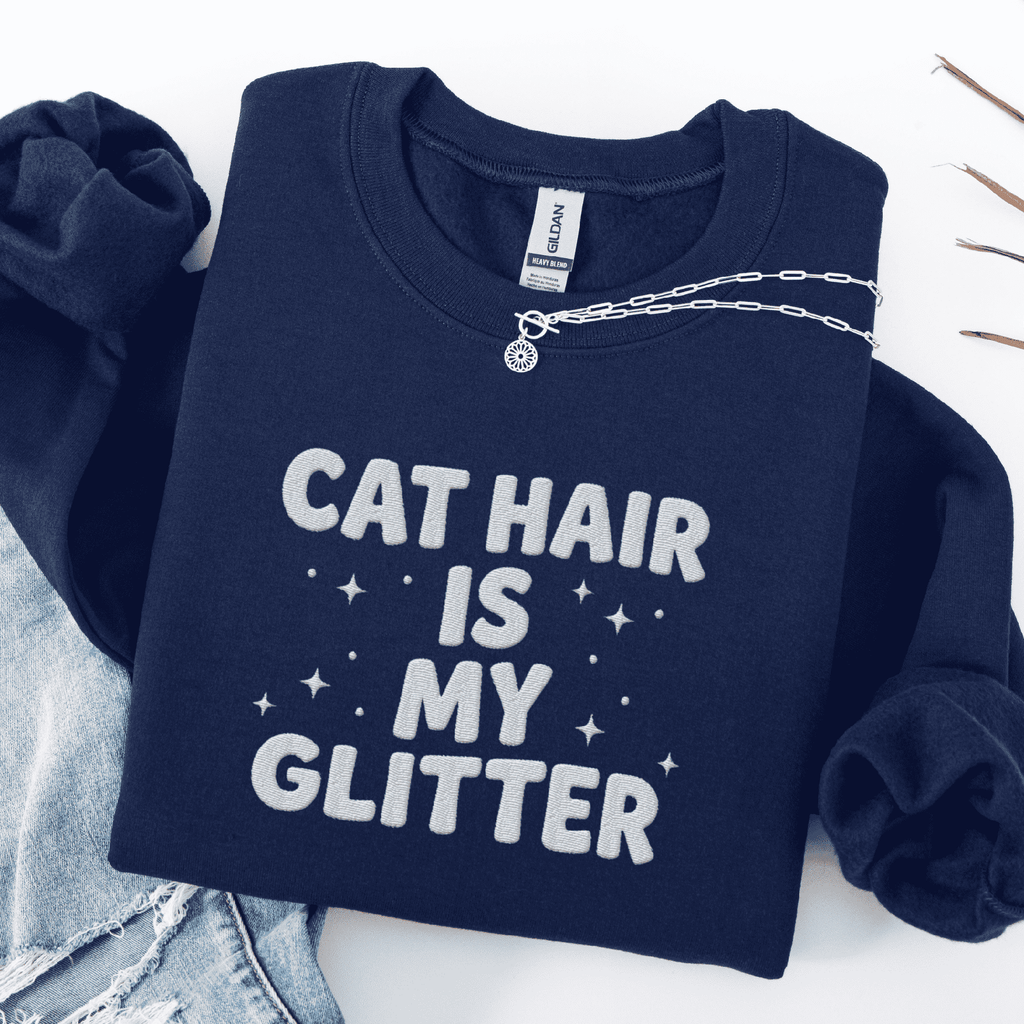 Navy cat embroidered sweatshirt with “Cat Hair Is My Glitter” text, folded flat on light denim