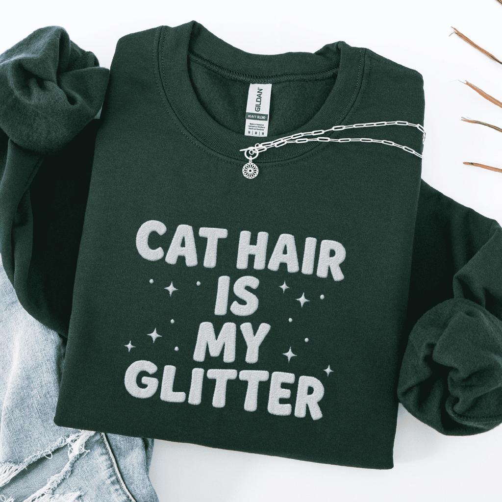 Forest Green cat embroidered sweatshirt with “Cat Hair Is My Glitter” text, folded flat on light denim