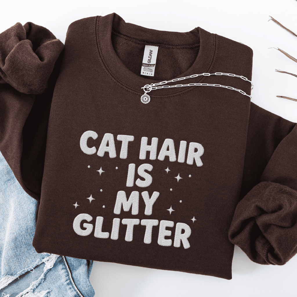 Dark Chocolate cat embroidered sweatshirt with “Cat Hair Is My Glitter” text, folded flat on light denim