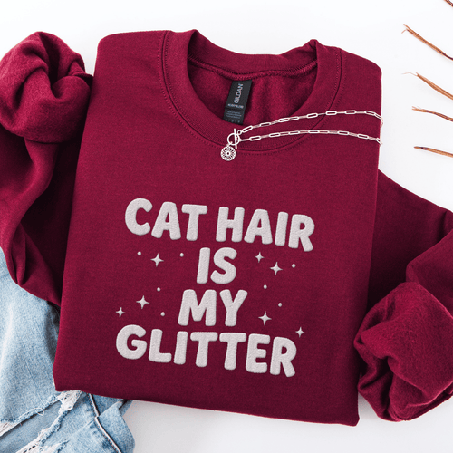 Maroon cat embroidered sweatshirt with “Cat Hair Is My Glitter” text, folded flat on light denim