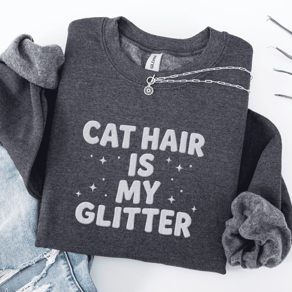 Dark Heather cat embroidered sweatshirt with “Cat Hair Is My Glitter” text, folded flat on light denim