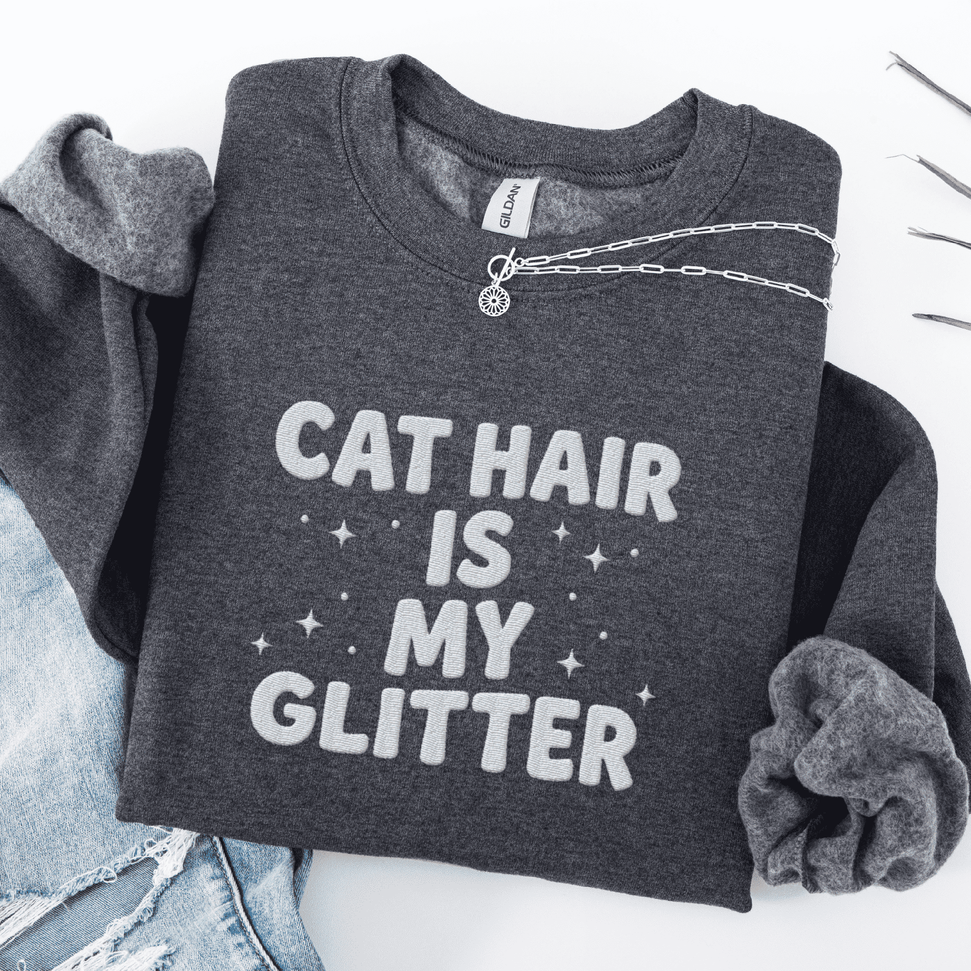 Dark Heather cat embroidered sweatshirt with “Cat Hair Is My Glitter” text, folded flat on light denim