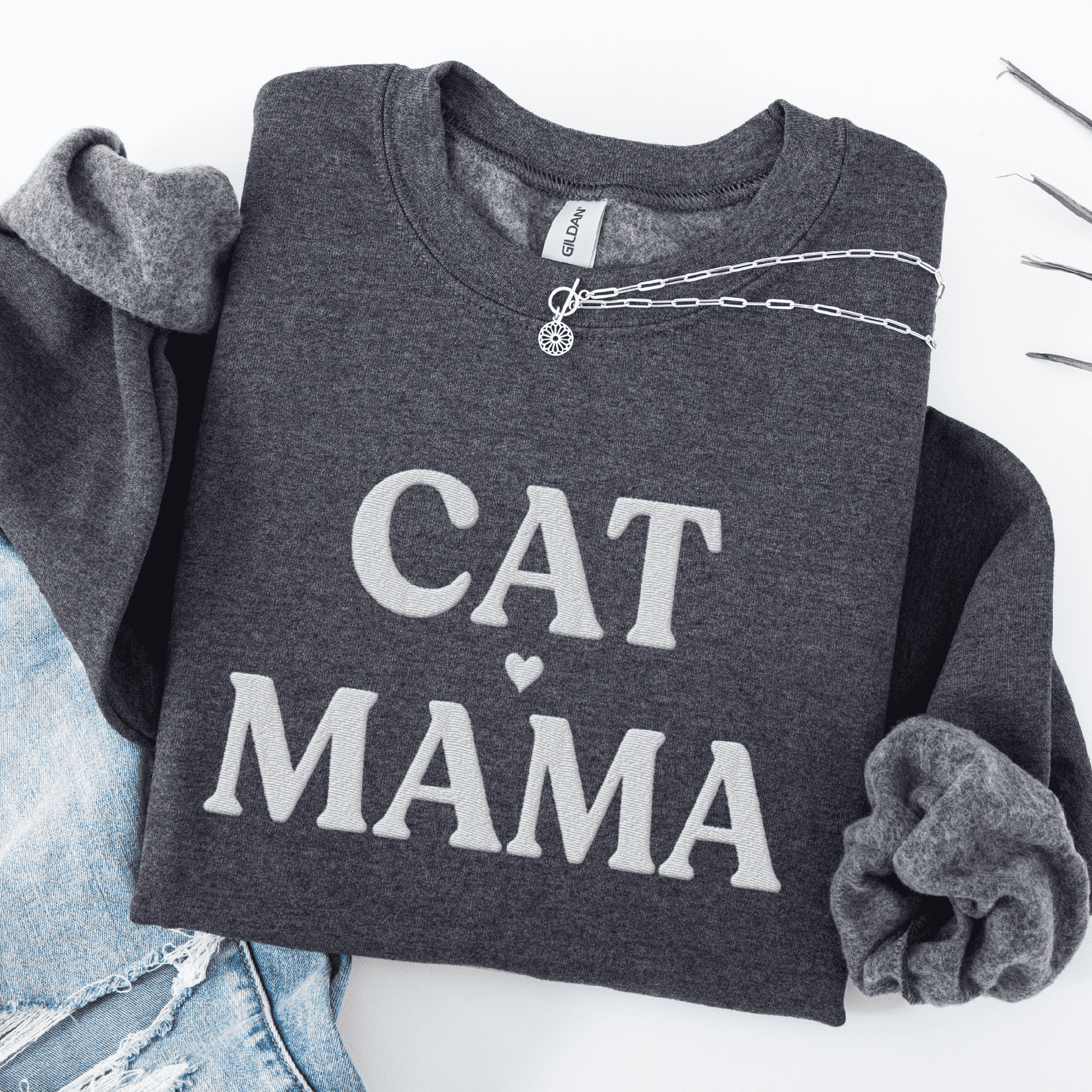 Maroon cat mama embroidered sweatshirt, folded flat on light denim