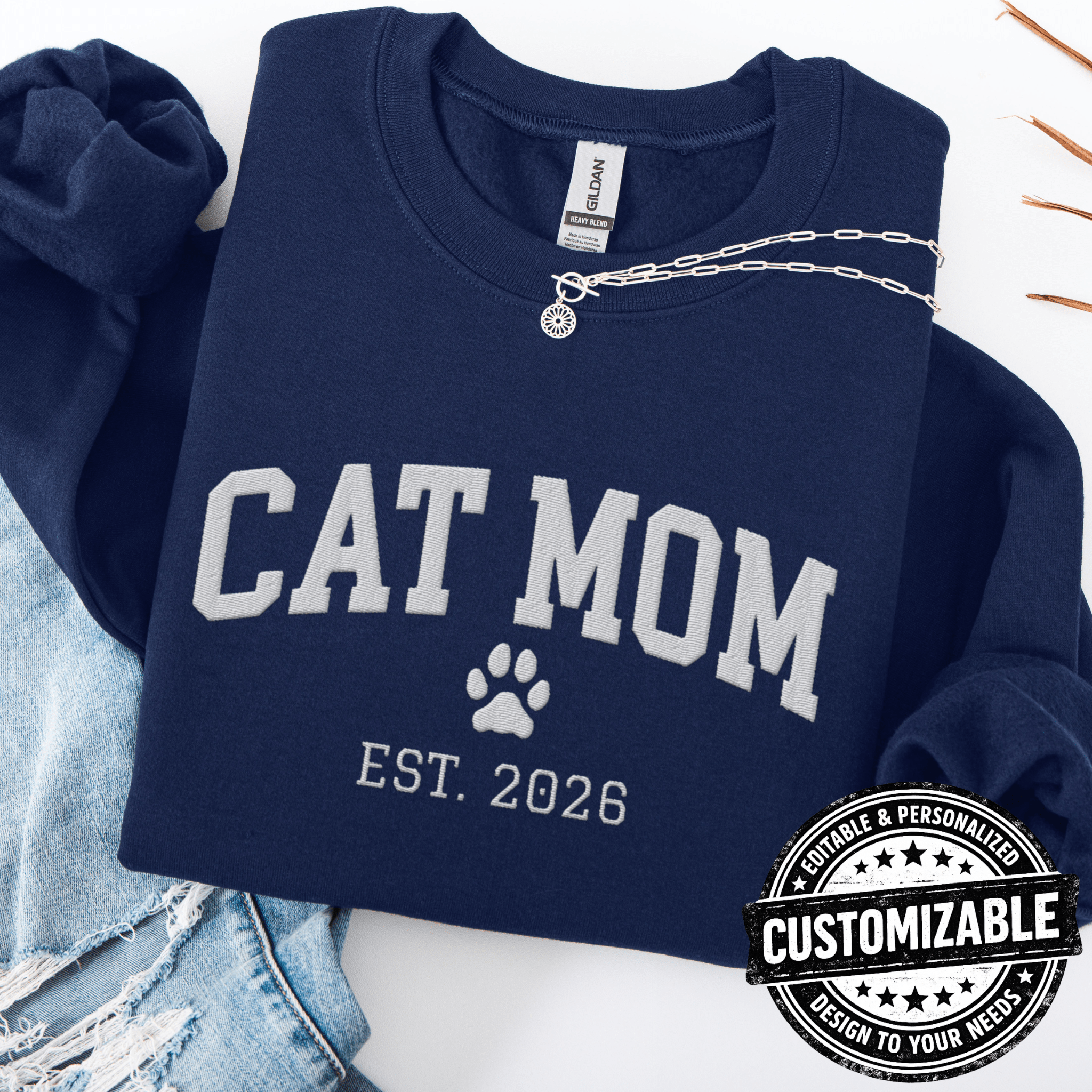 Navy customizable cat mom embroidered sweatshirt with paw print and custom year detail, folded flat on light denim