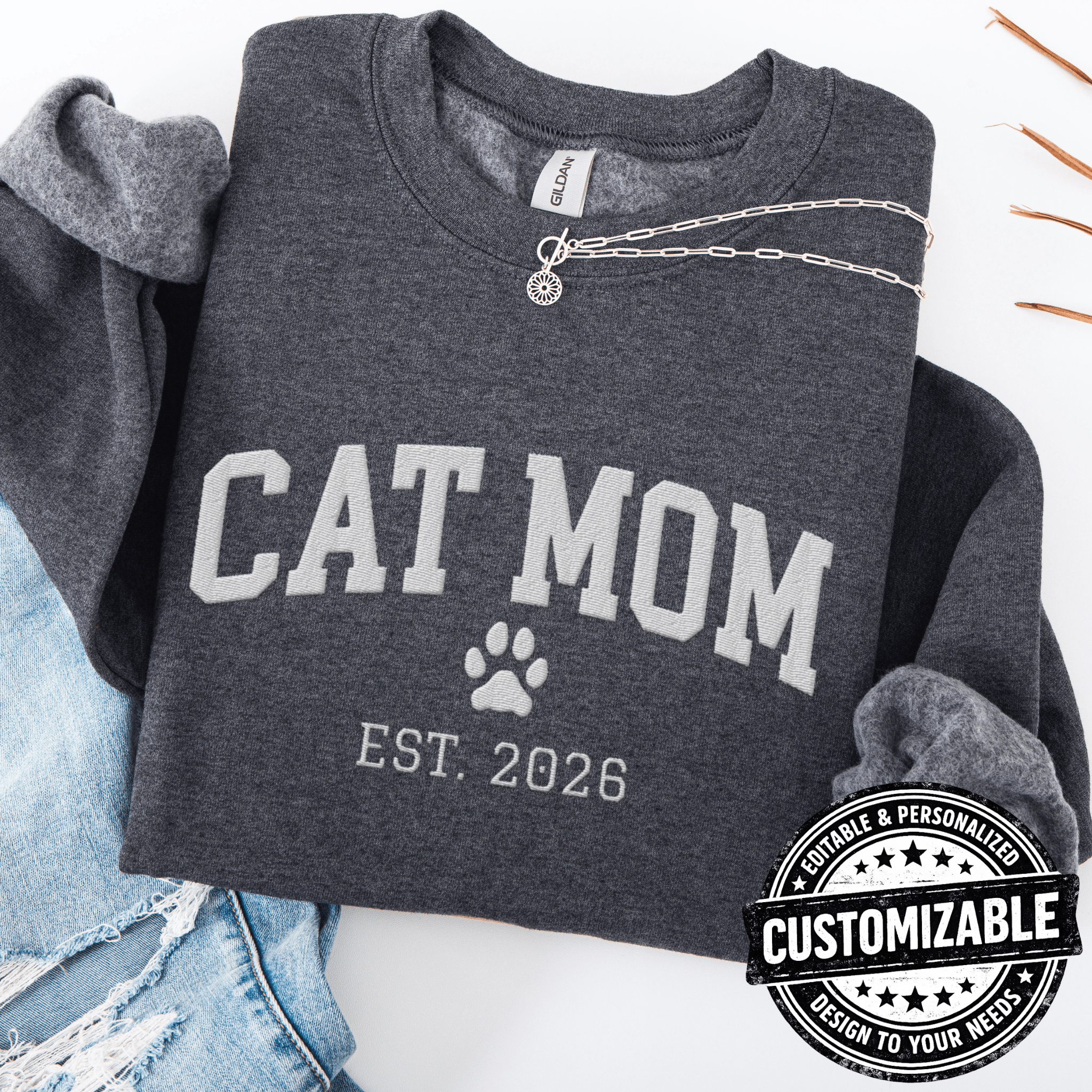 Dark Heather customizable cat mom embroidered sweatshirt with paw print and custom year detail, folded flat on light denim