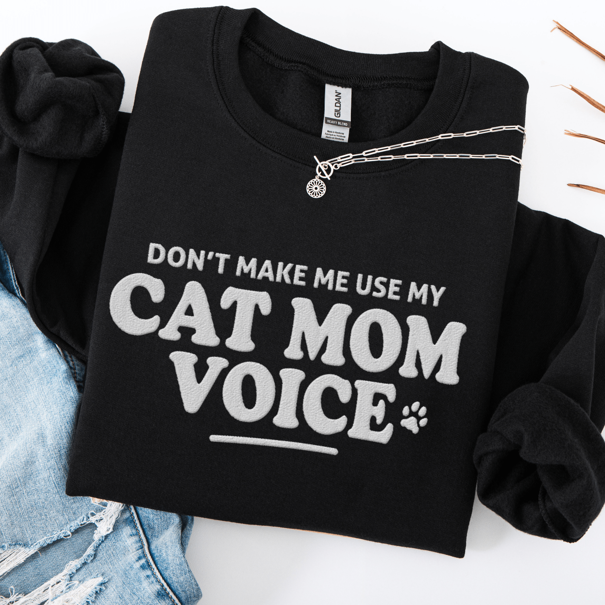 Black cat mom embroidered sweatshirt with “Don’t Make Me Use My Cat Mom Voice” text, folded flat on light denim