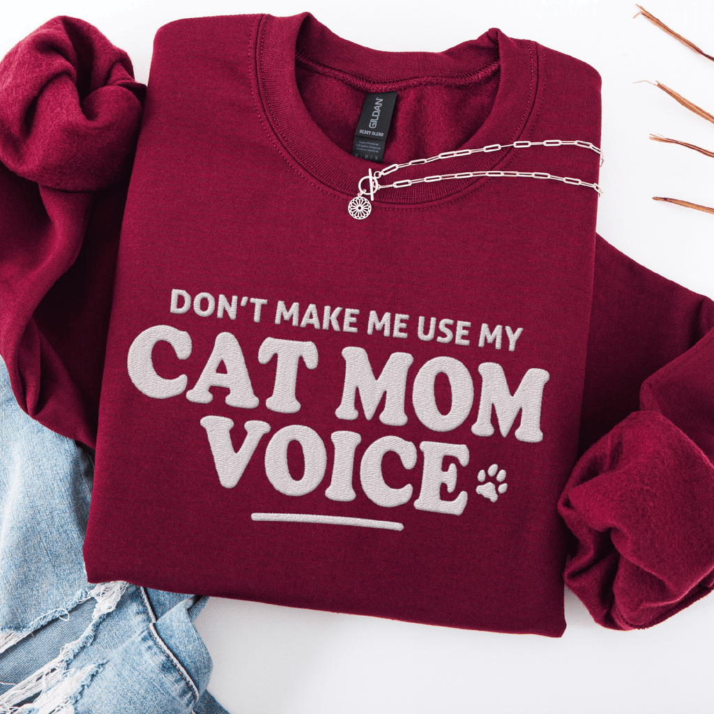 Maroon cat mom embroidered sweatshirt with “Don’t Make Me Use My Cat Mom Voice” text, folded flat on light denim