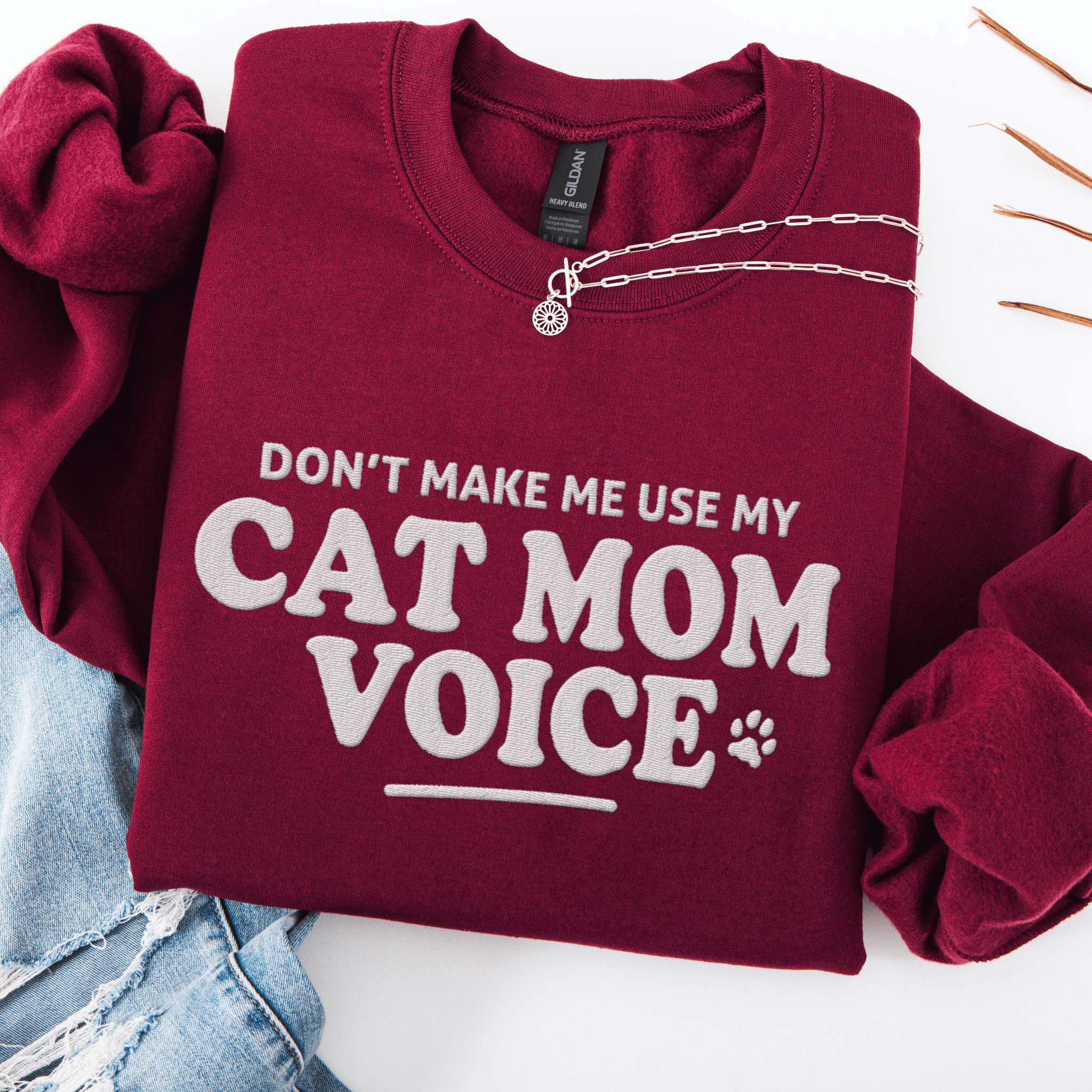 Maroon cat mom embroidered sweatshirt with “Don’t Make Me Use My Cat Mom Voice” text, folded flat on light denim