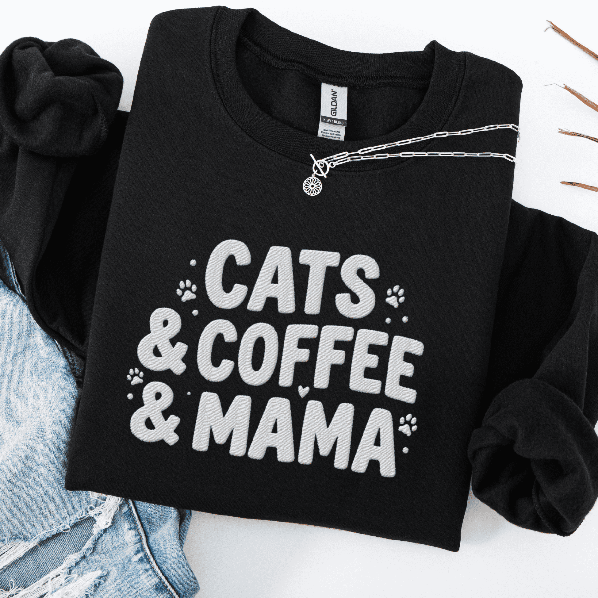 Black cats coffee mama embroidered sweatshirt with paw print detail, folded flat on light denim