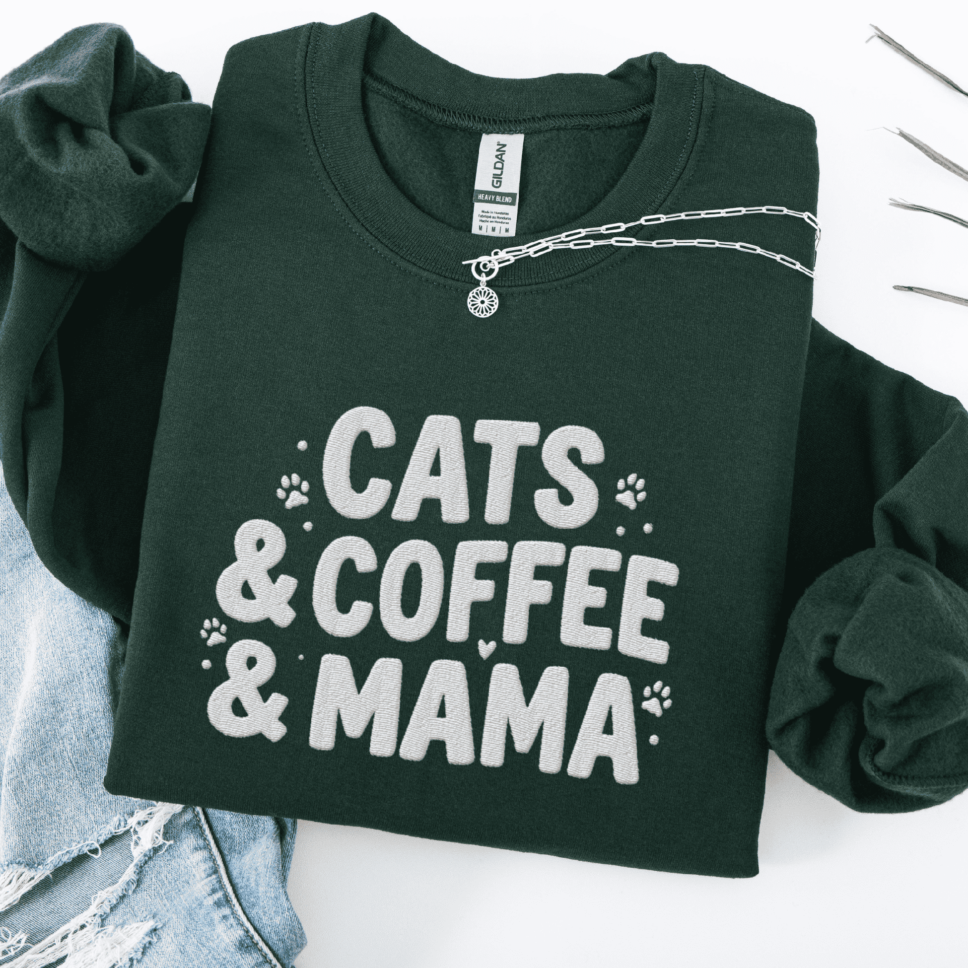 Forest Green cats coffee mama embroidered sweatshirt with paw print detail, folded flat on light denim