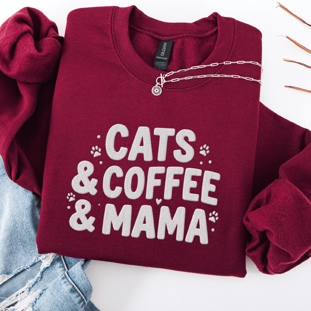Maroon cats coffee mama embroidered sweatshirt with paw print detail, folded flat on light denim