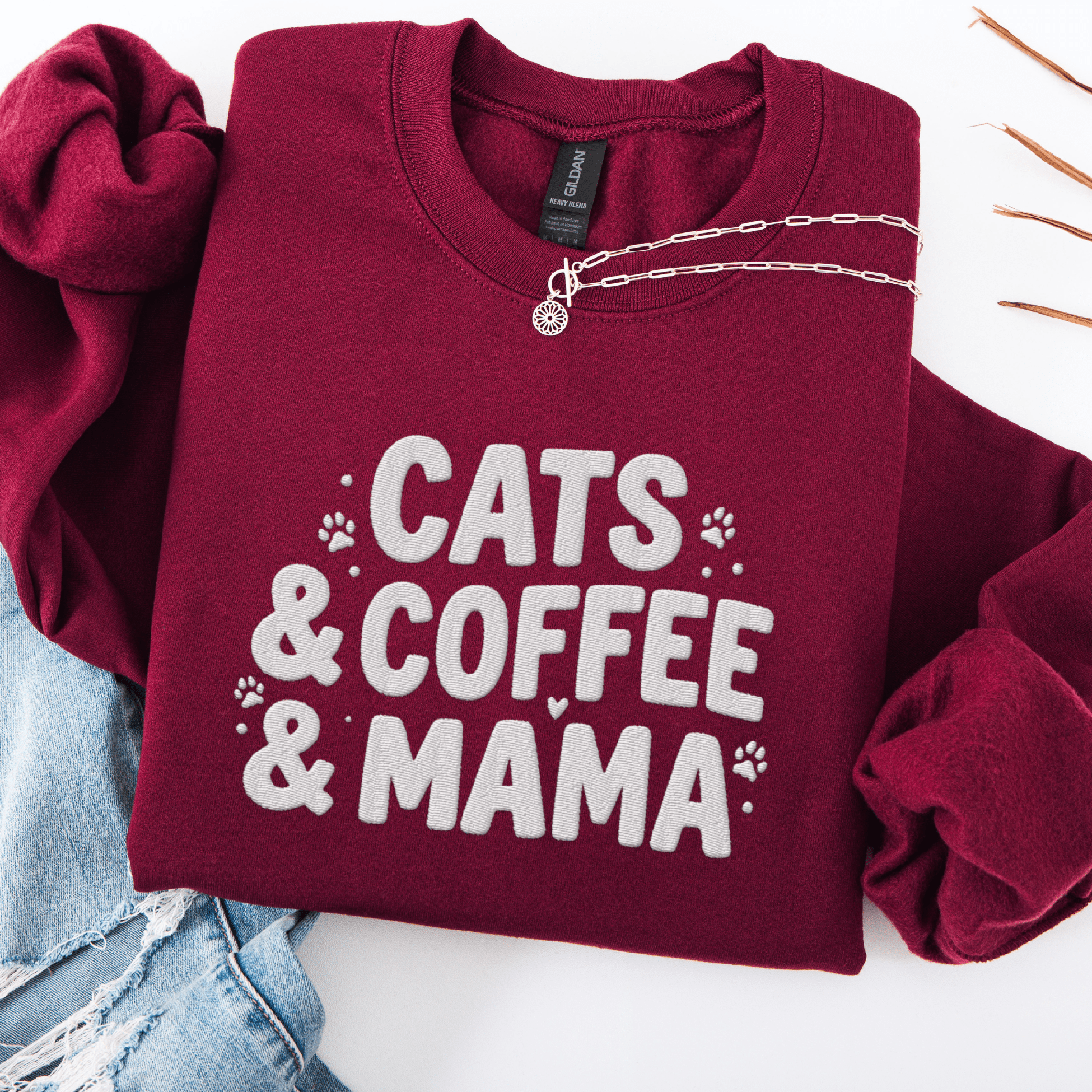 Maroon cats coffee mama embroidered sweatshirt with paw print detail, folded flat on light denim