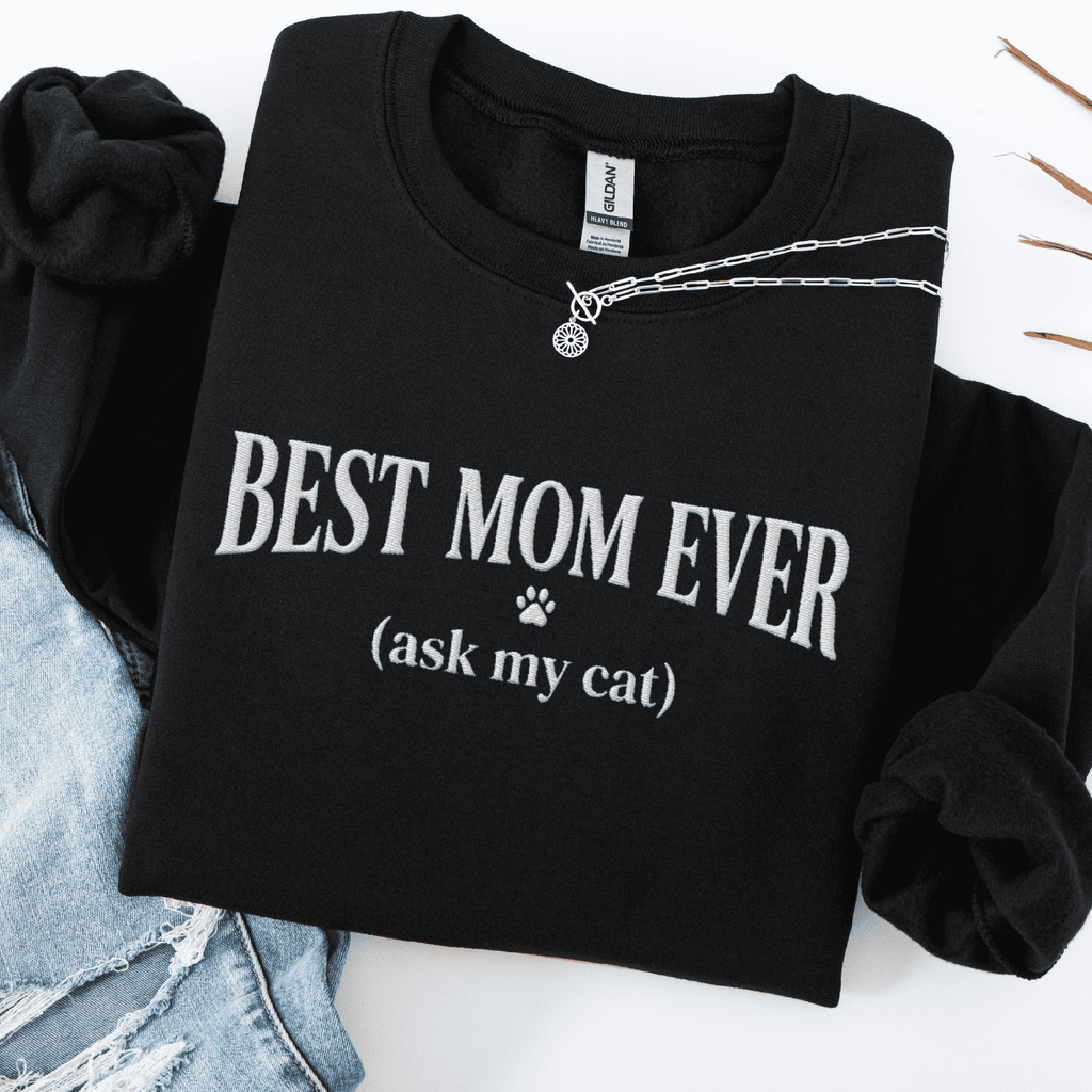 Black cat mom embroidered sweatshirt with “Best Mom Ever (ask my cat)” text, folded flat on light denim