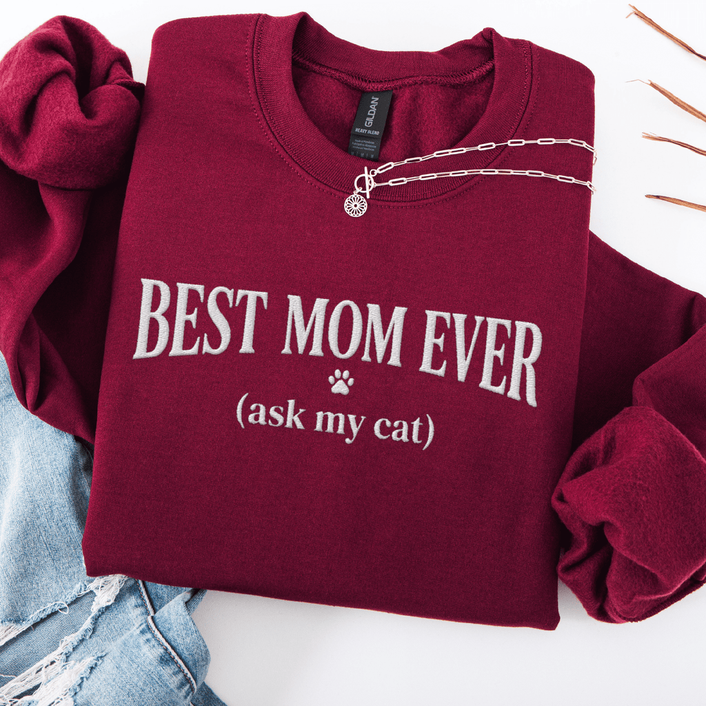 Maroon cat mom embroidered sweatshirt with “Best Mom Ever (ask my cat)” text, folded flat on light denim