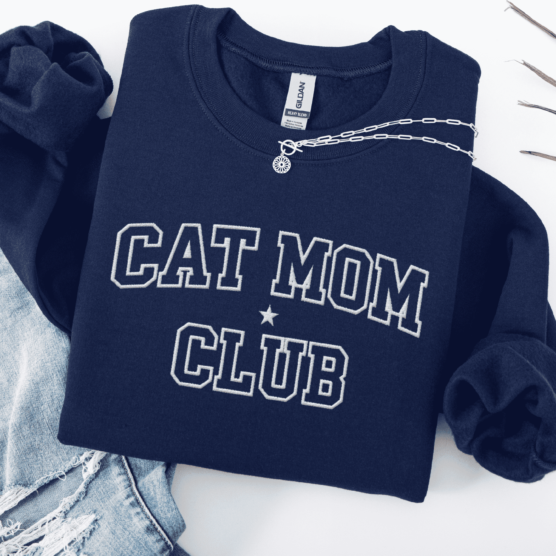 Navy cat mom club embroidered sweatshirt, folded flat on light denim
