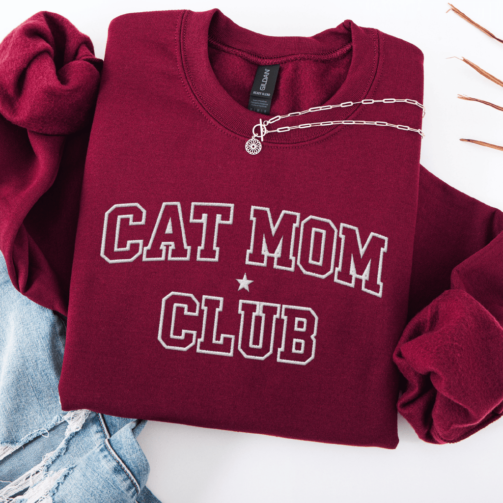 Maroon cat mom club embroidered sweatshirt, folded flat on light denim
