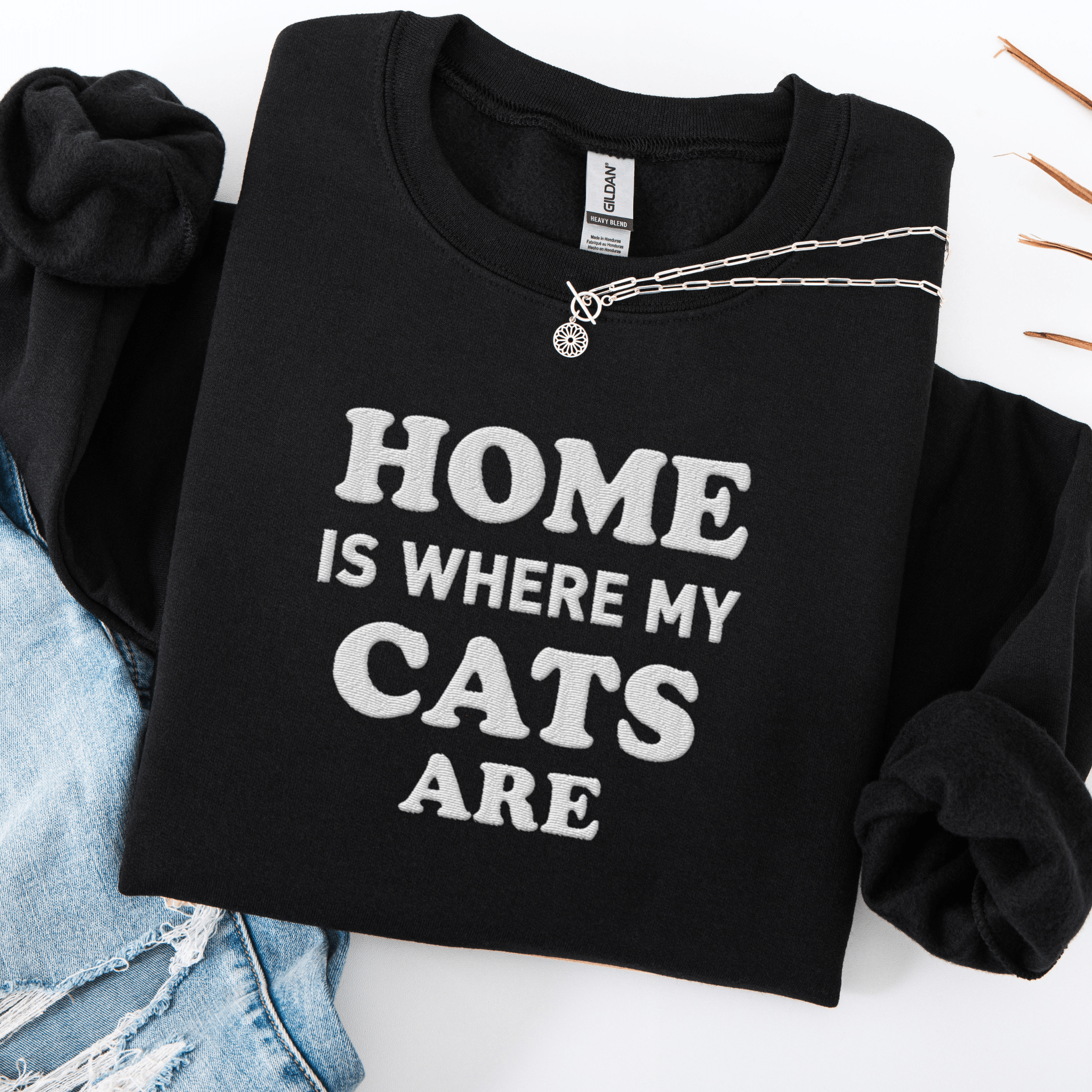 Black cat embroidered sweatshirt with “Home Is Where My Cats Are” text, folded flat on light denim