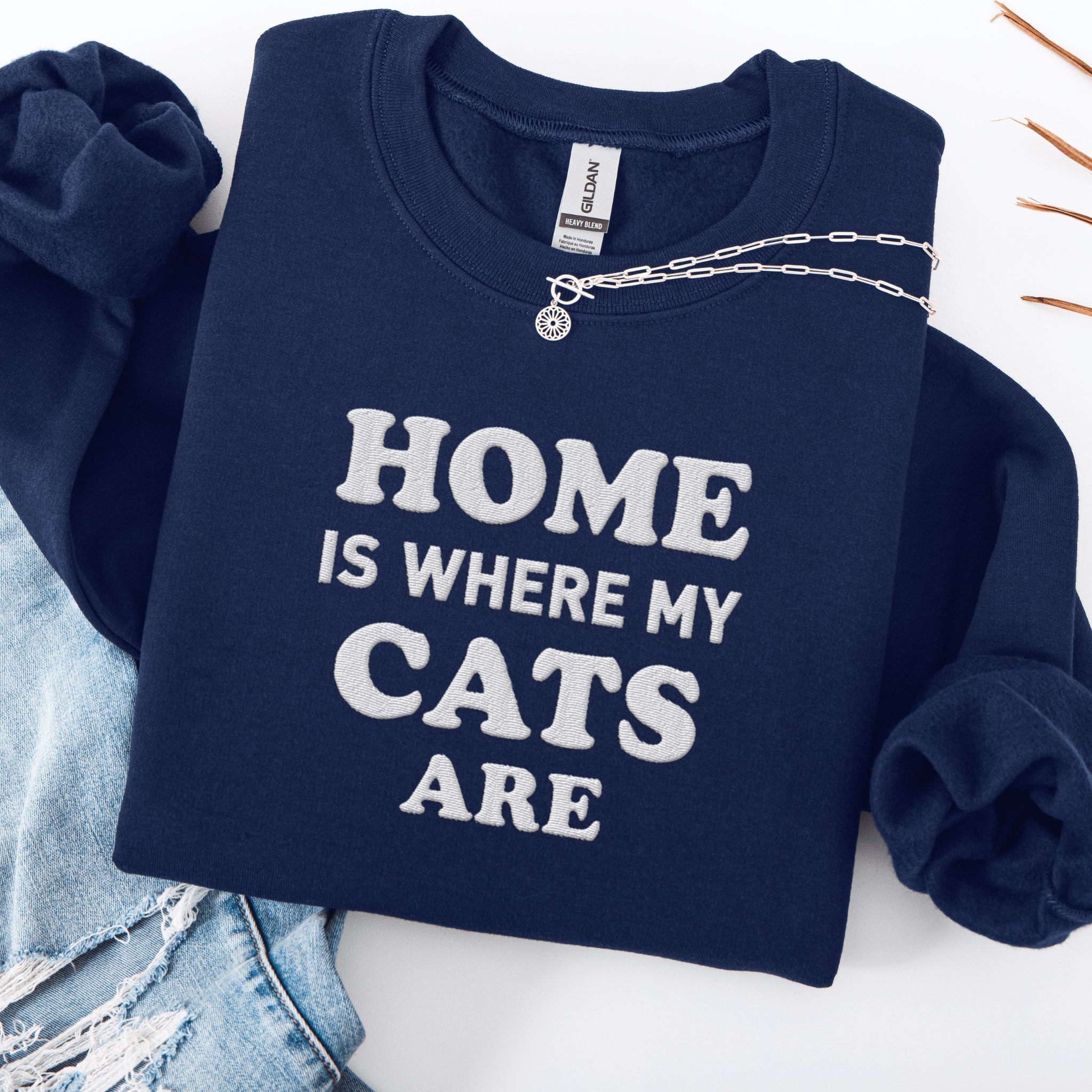Navy cat embroidered sweatshirt with “Home Is Where My Cats Are” text, folded flat on light denim