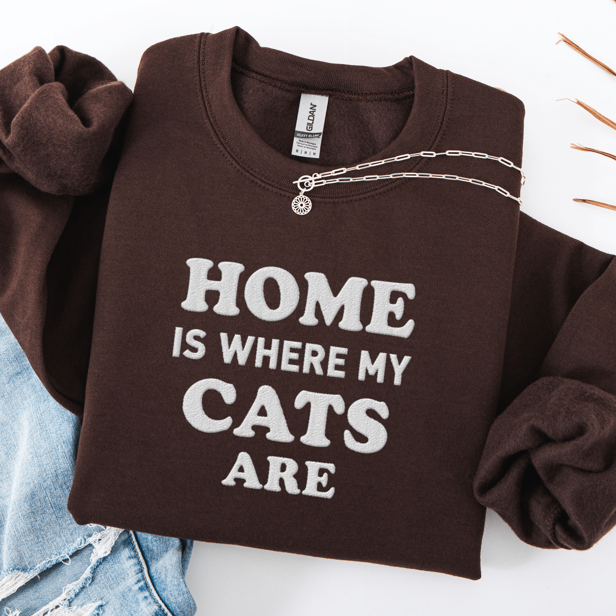 Dark Chocolate cat embroidered sweatshirt with “Home Is Where My Cats Are” text, folded flat on light denim
