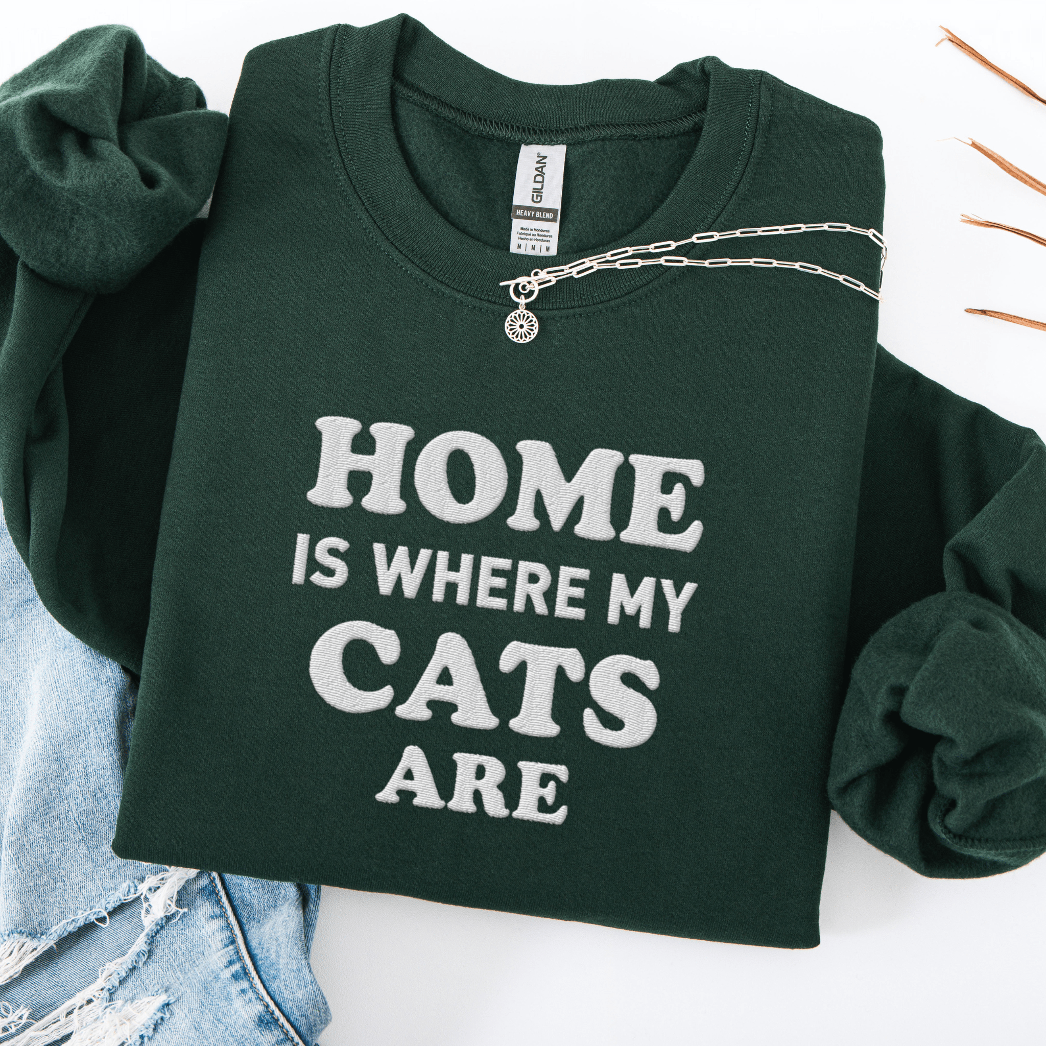 Forest Green cat embroidered sweatshirt with “Home Is Where My Cats Are” text, folded flat on light denim