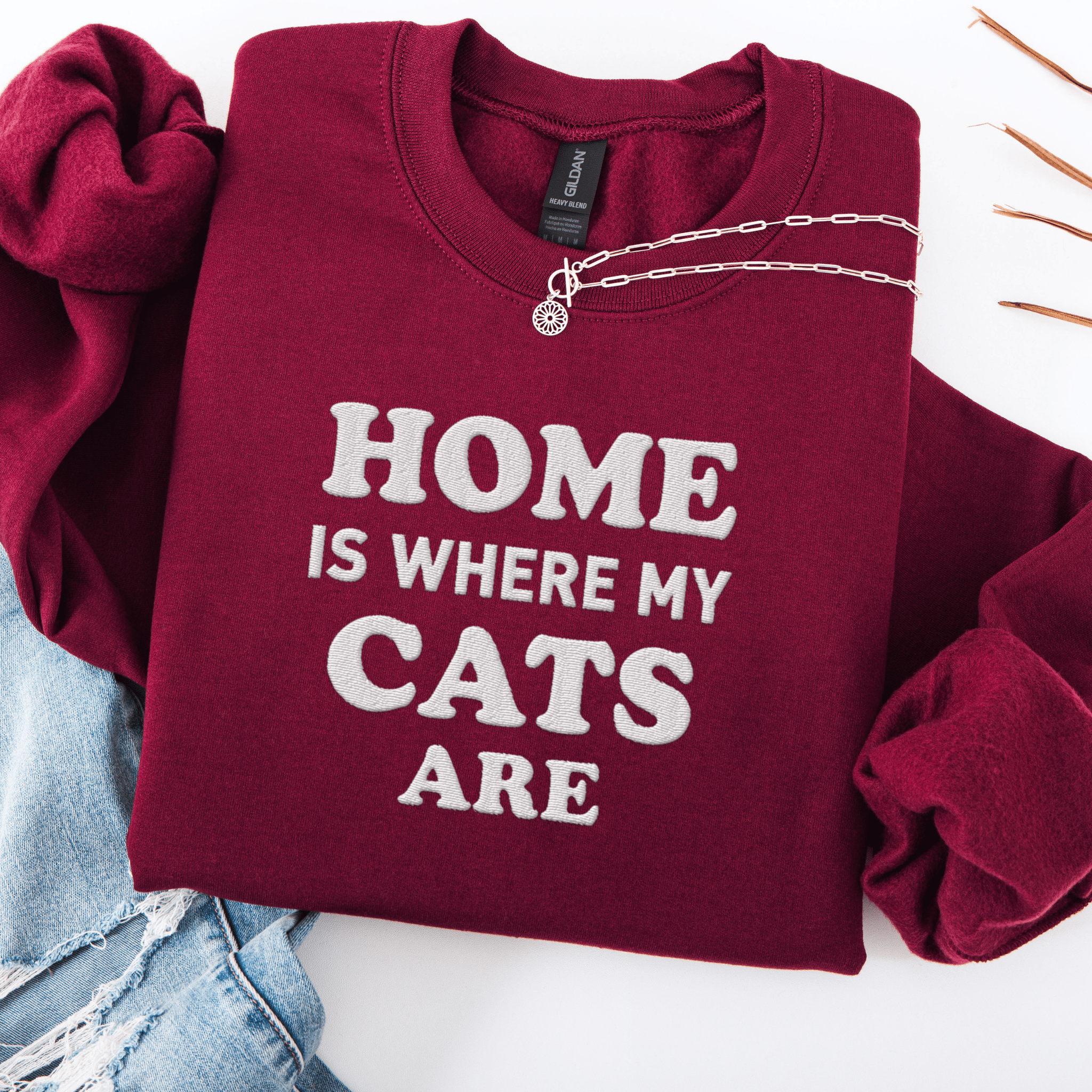 Maroon cat embroidered sweatshirt with “Home Is Where My Cats Are” text, folded flat on light denim